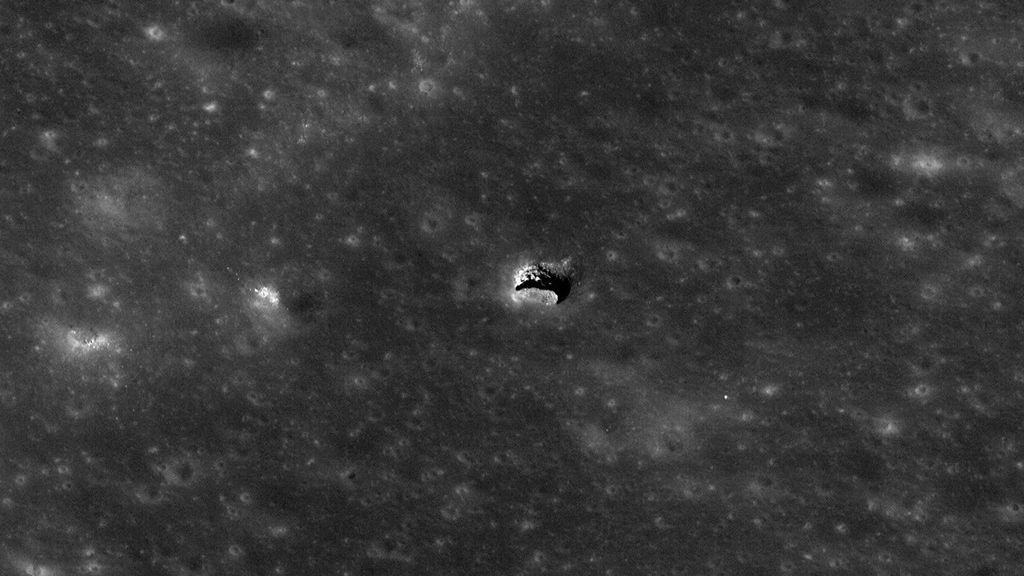 Imagen de satélite de la superficie de la Luna. En el centro de la imagen, la superficie es interrumpida bruscamente por lo que parece ser una abertura en el techo de una cueva. El paisaje está iluminado en un ángulo bajo, revelando una pequeña parte de lo que parece ser un vacío mayor debajo de la abertura.