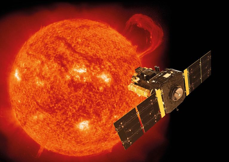 A spacecraft appears in the foreground on the right, while the Sun appears in orange in the background on the left.