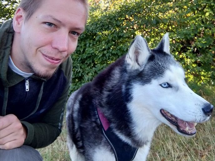 Timo kneels beside a gray and white Husky dog.