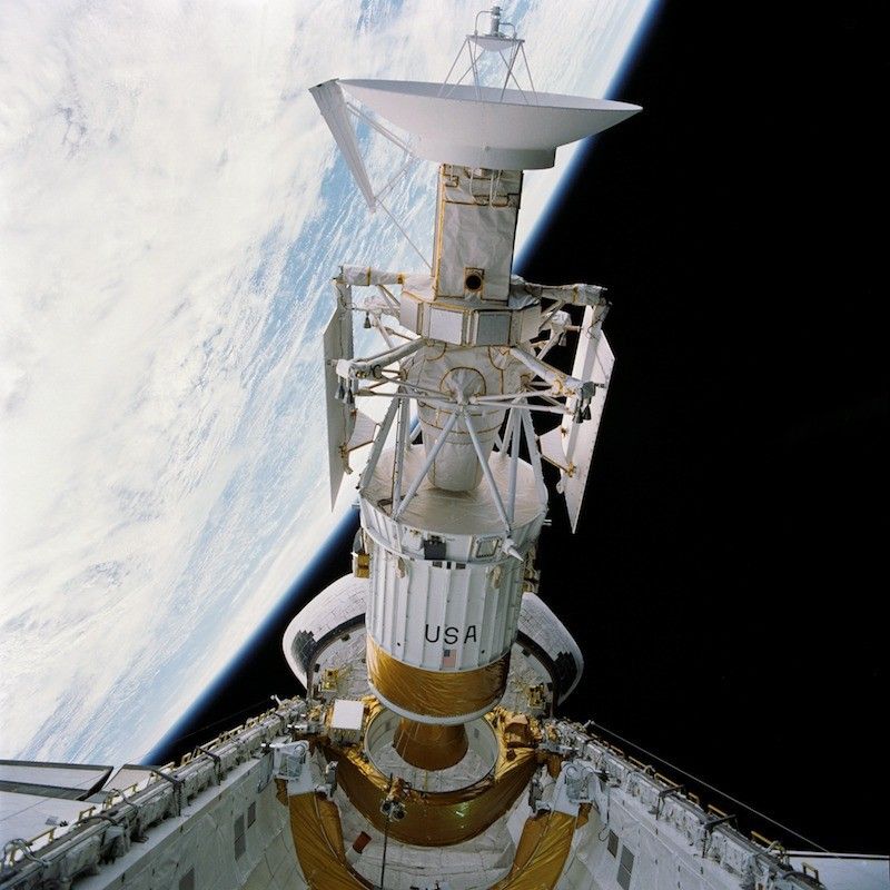 A long cylindrical spacecraft with an antenna dish on one end emerges from the cargo bay of the Space Shuttle.