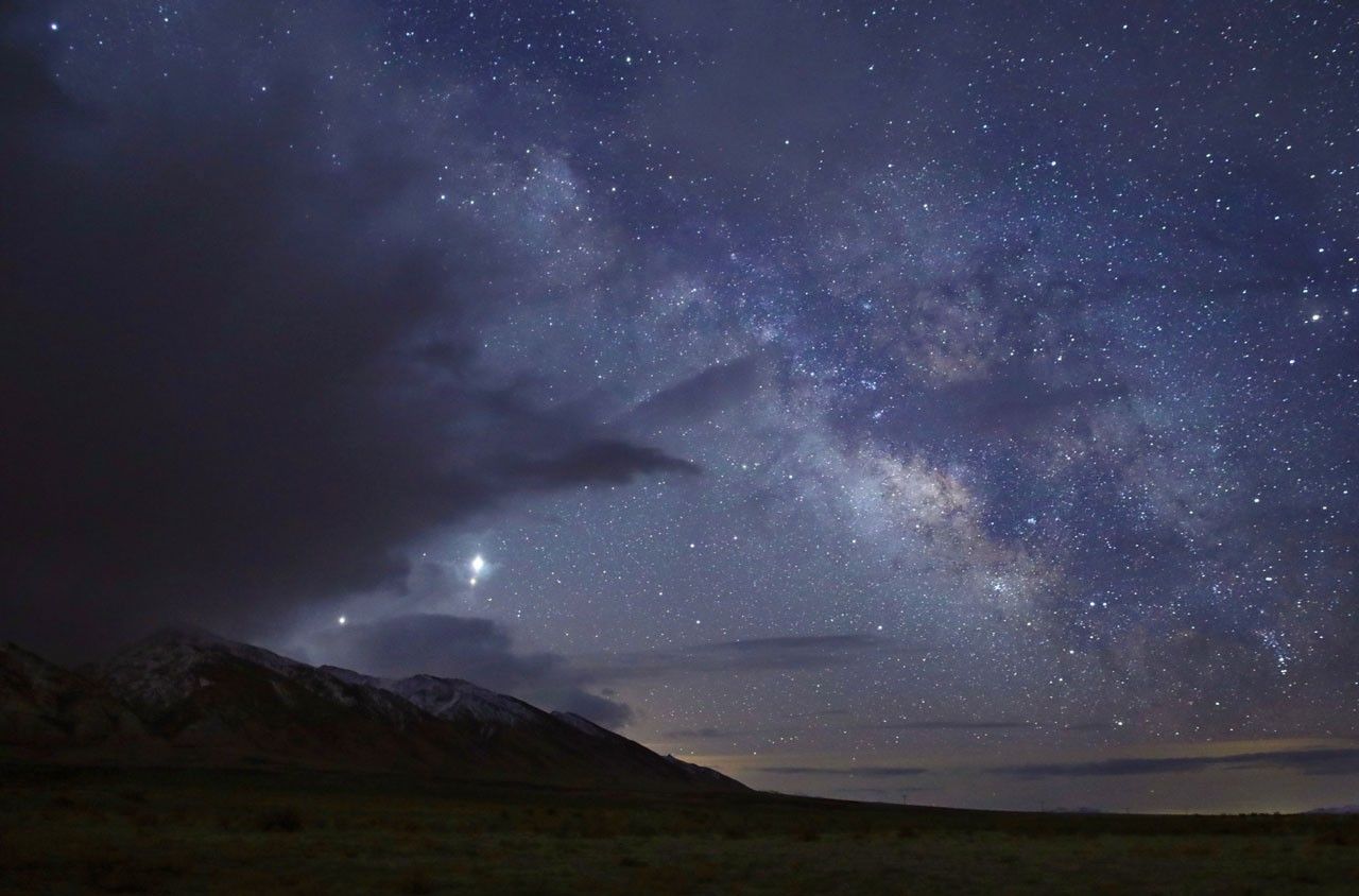 Three planets stand out among a twilight sky filled with stars over snow-capped mountains.