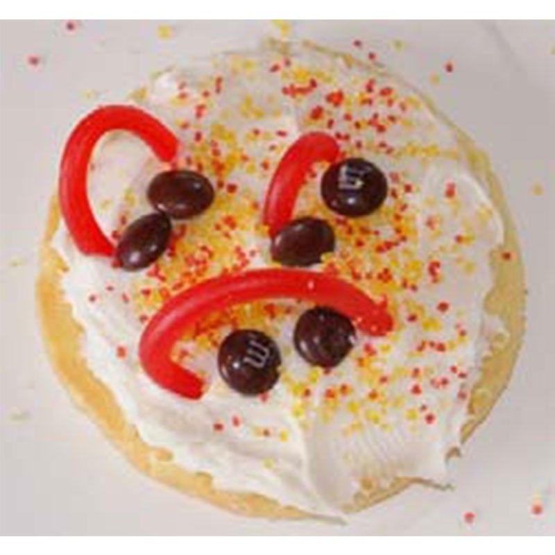 A cookie covered in white frosting, yellow and red sprinkles, brown M&M's, and red licorice.