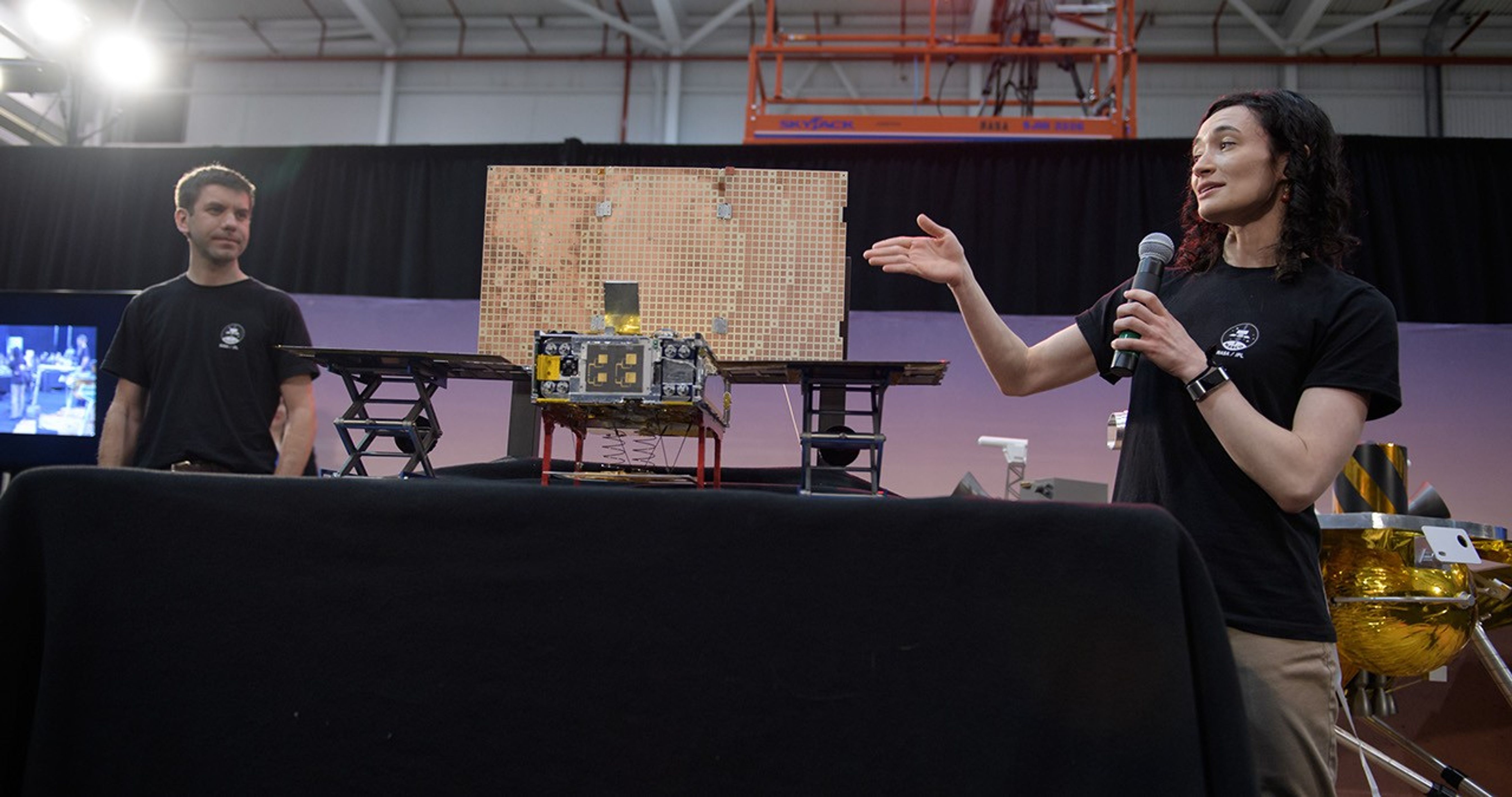 Man and woman standing next to MarCo cubesat.