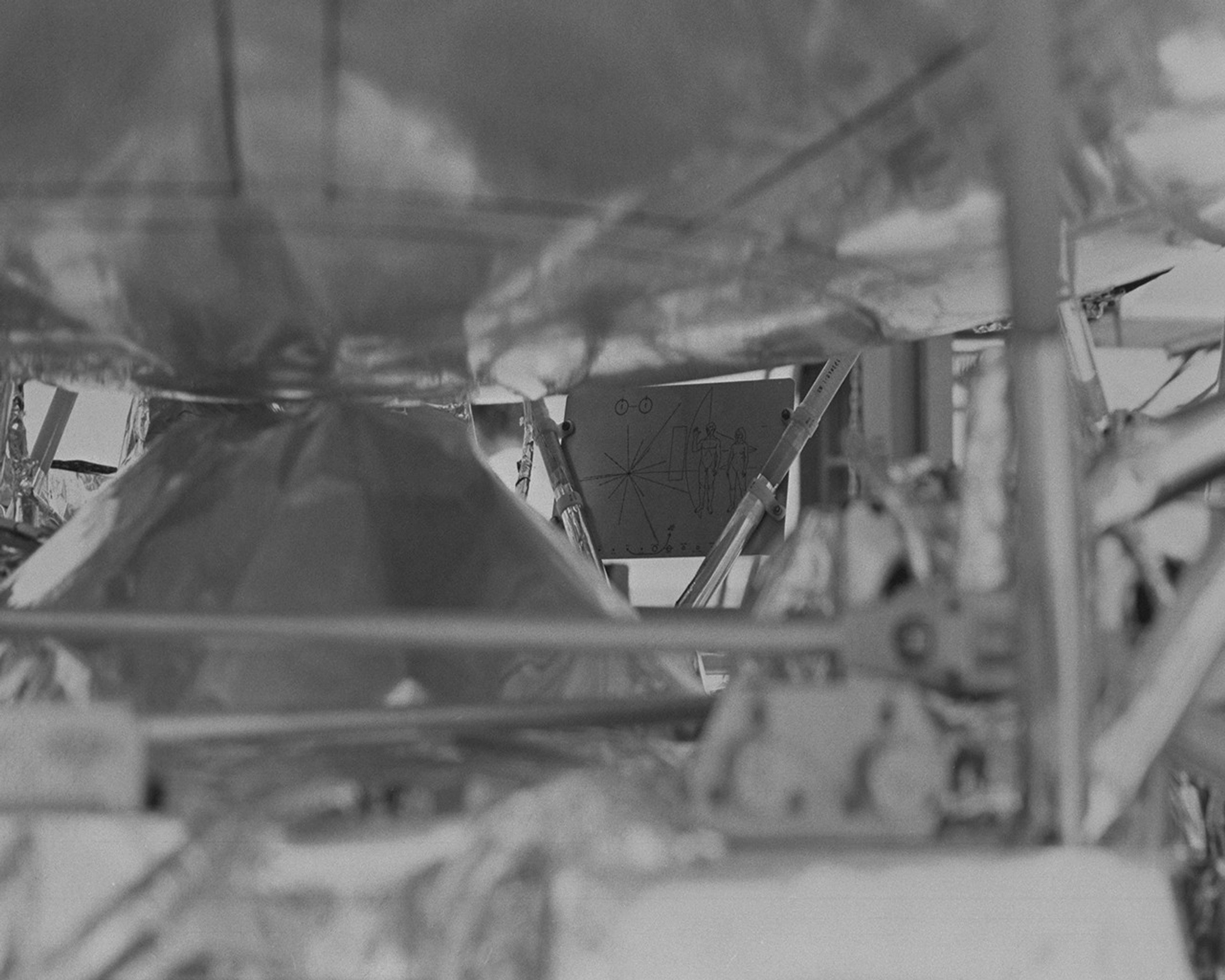 Black and white image of plaque with illustrations on it mounted to spacecraft.