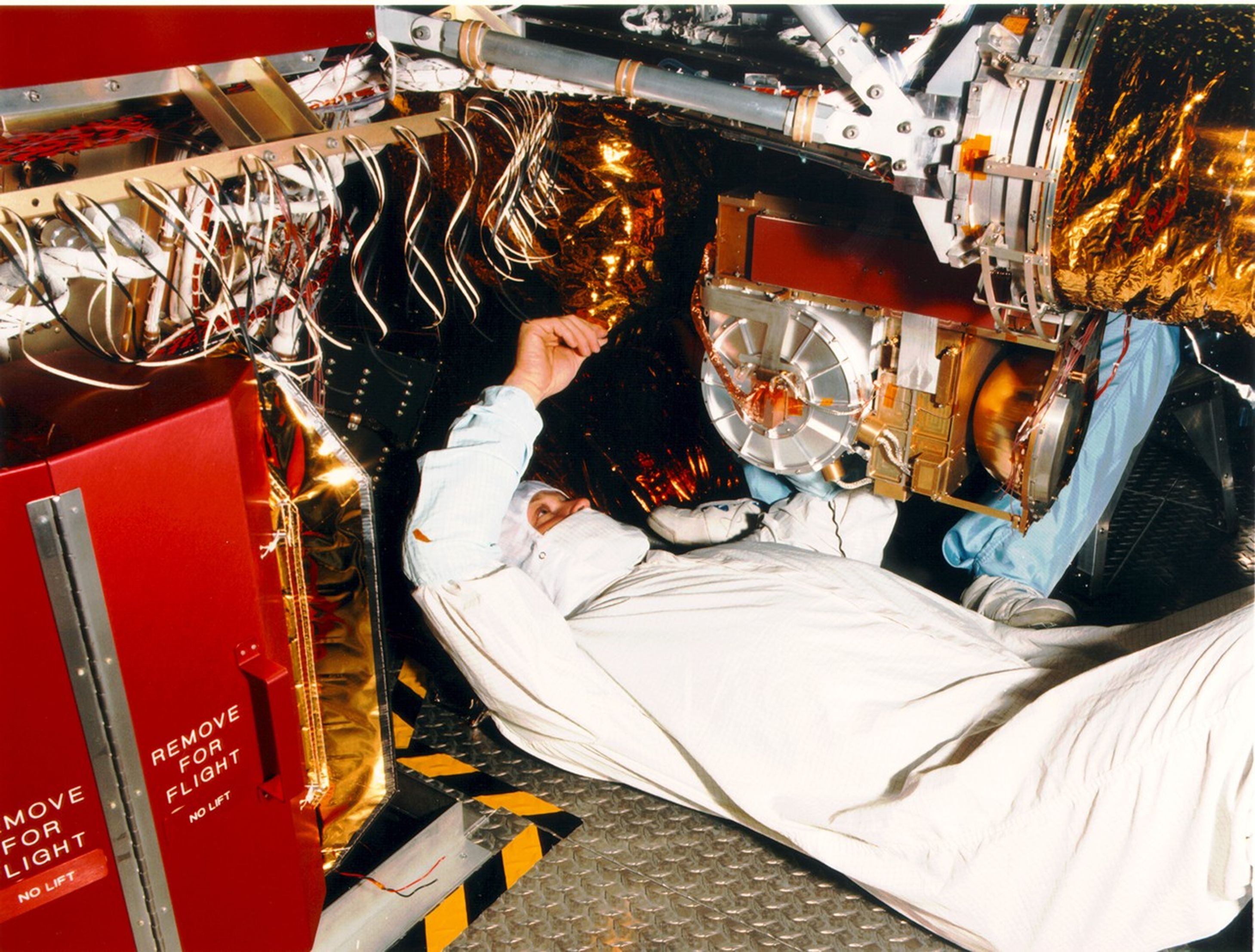 Color image of man on his back working on a spacecraft.