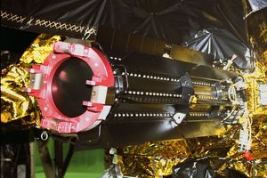 A large black cylinder with fins on the side is inserted into the side of a spacecraft.