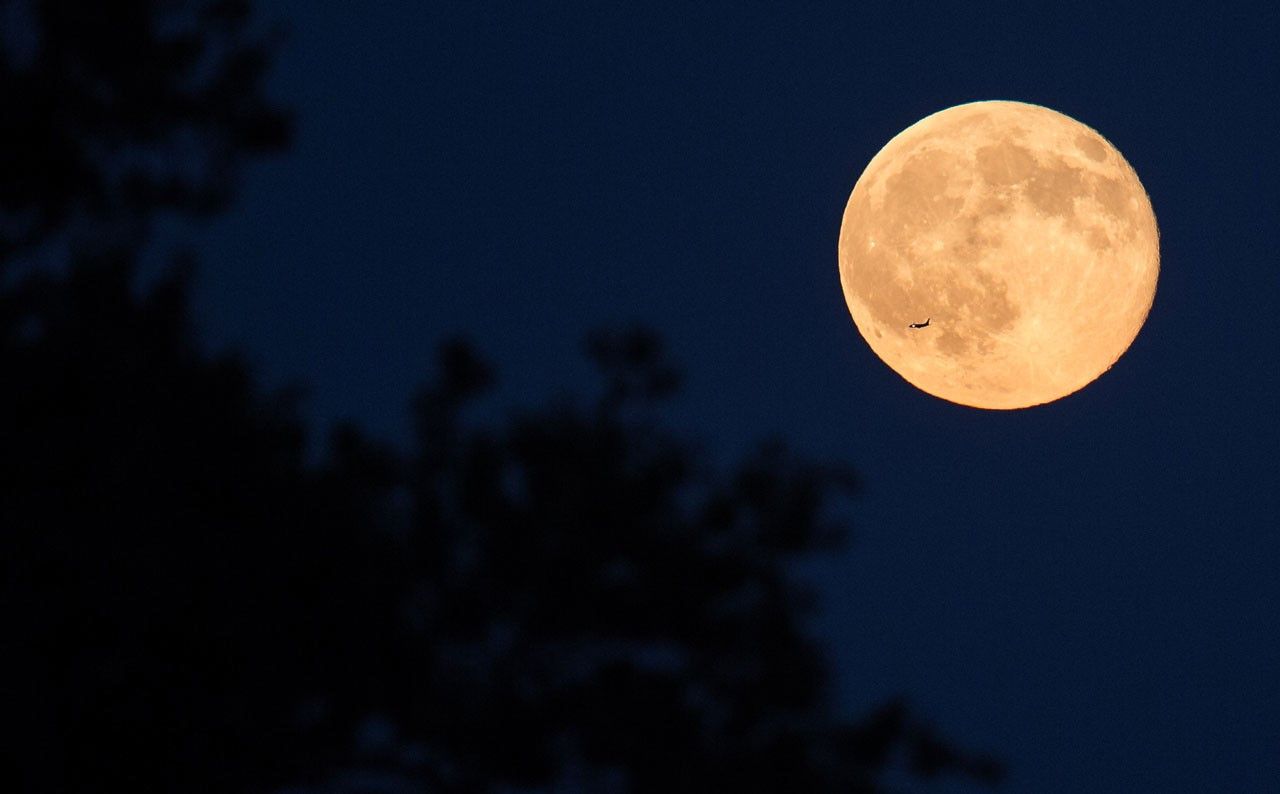 An airplane is silhouetted against the bright full Moon.