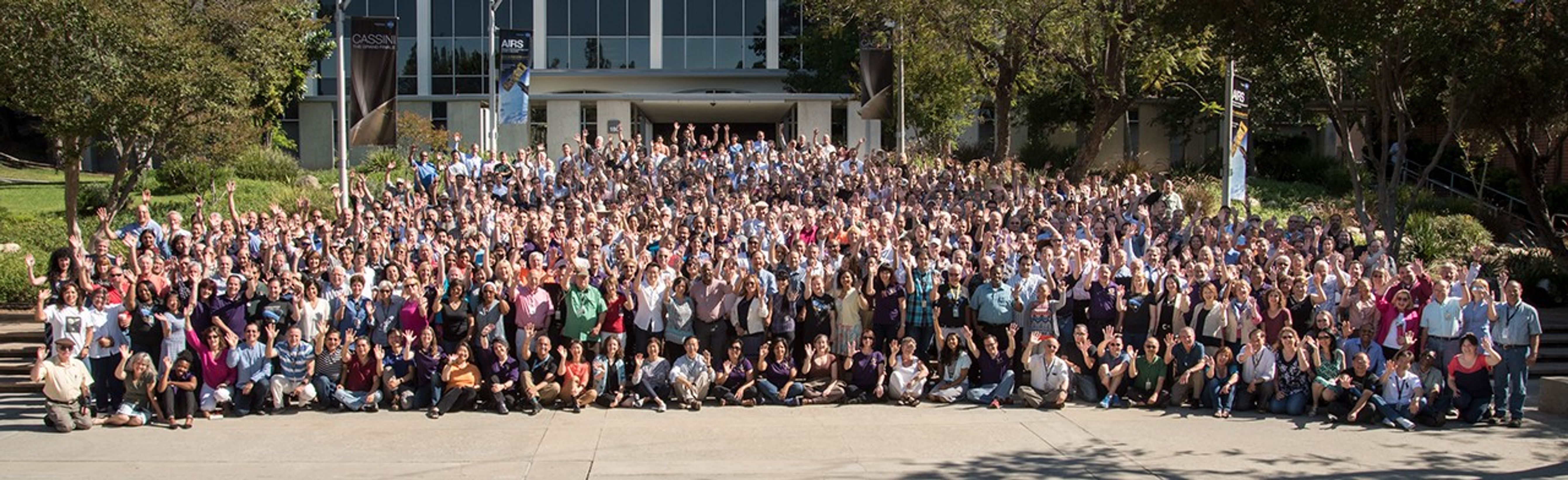 Color image of hundreds of people in front of a building waving at the camera.