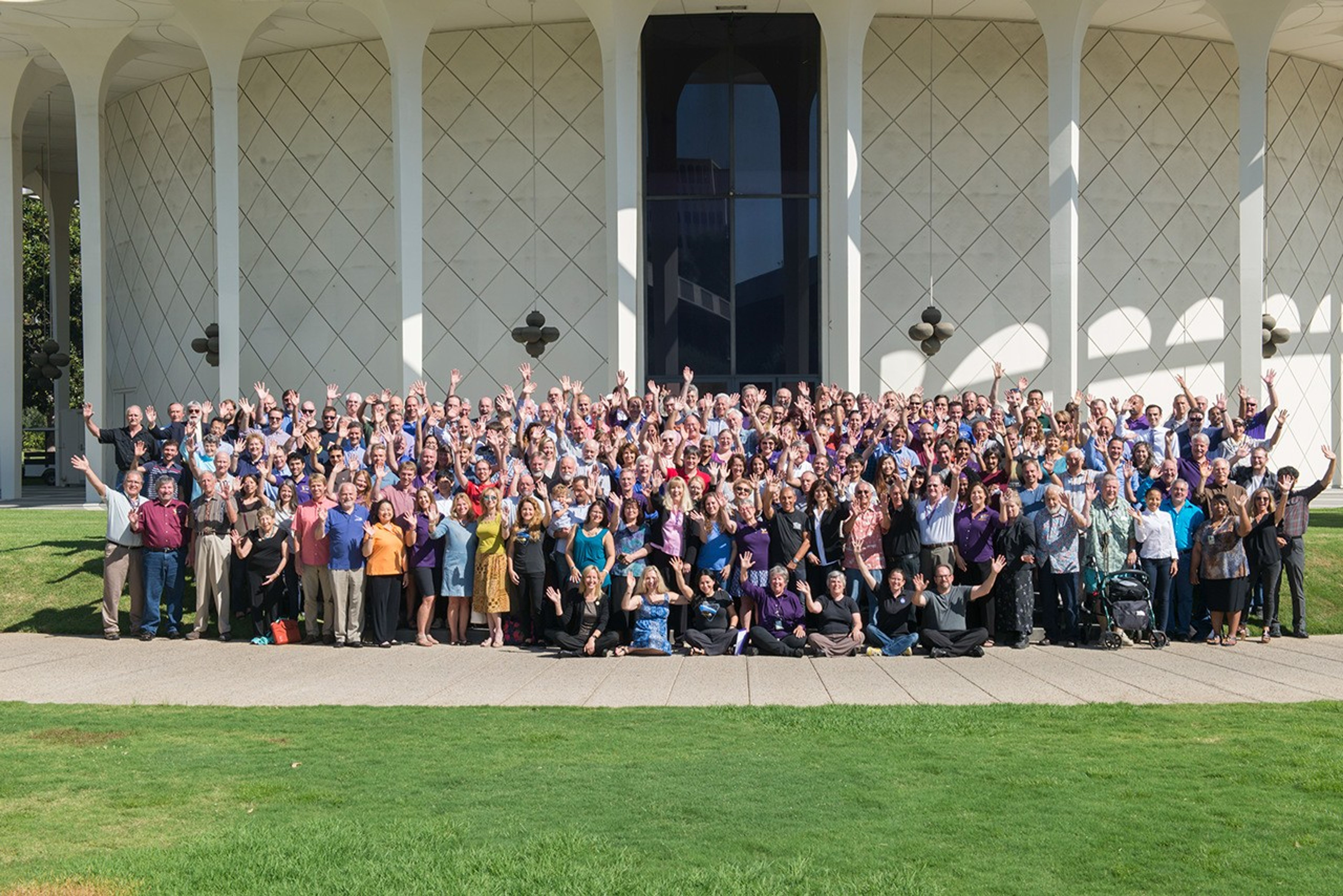 Color image of a large group of people smiling and waving.