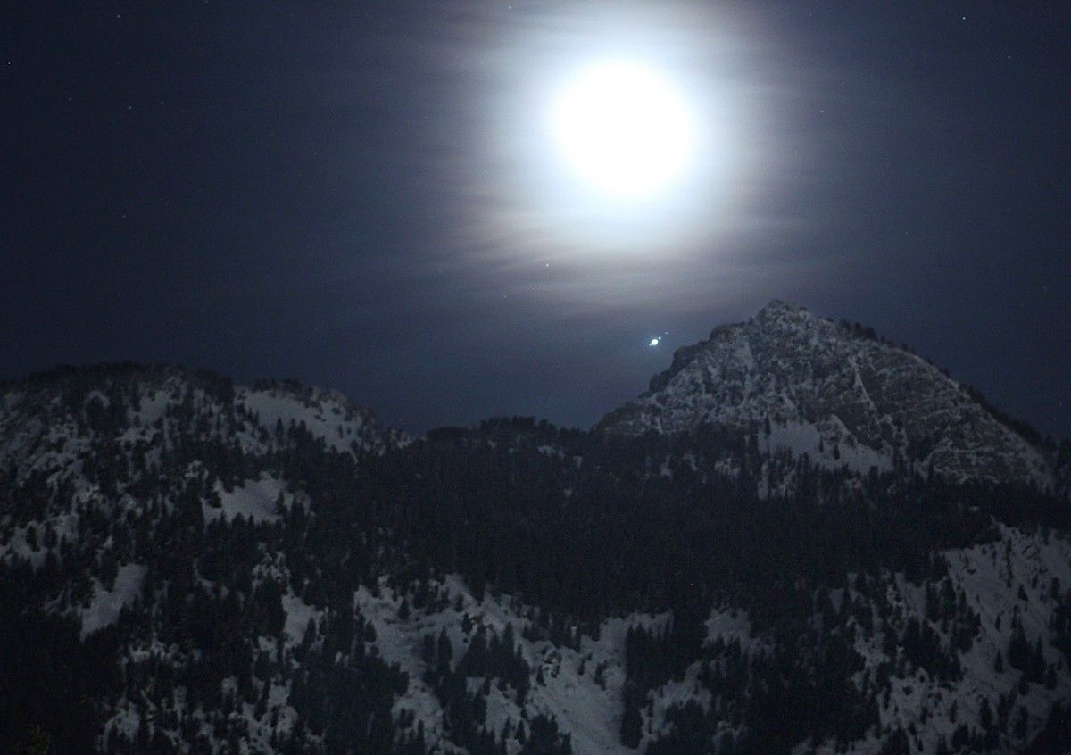 bright, hazy moon and stars above dark mountain range