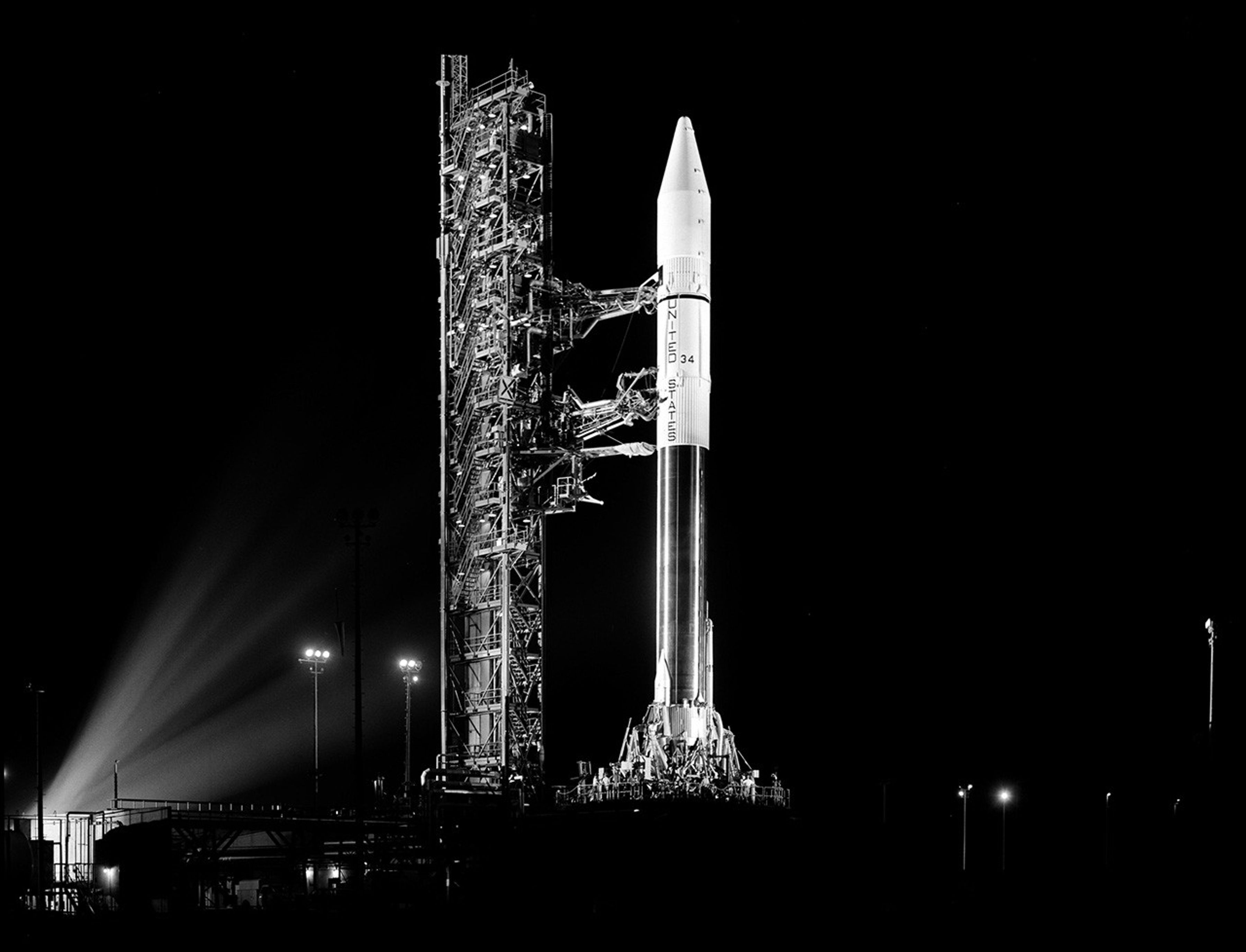 Rocket illuminated by spotlights on launch pad at night.