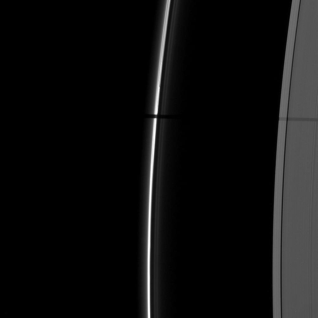 A wide shadow is cast onto the thin F ring and the A ring by the moon Janus