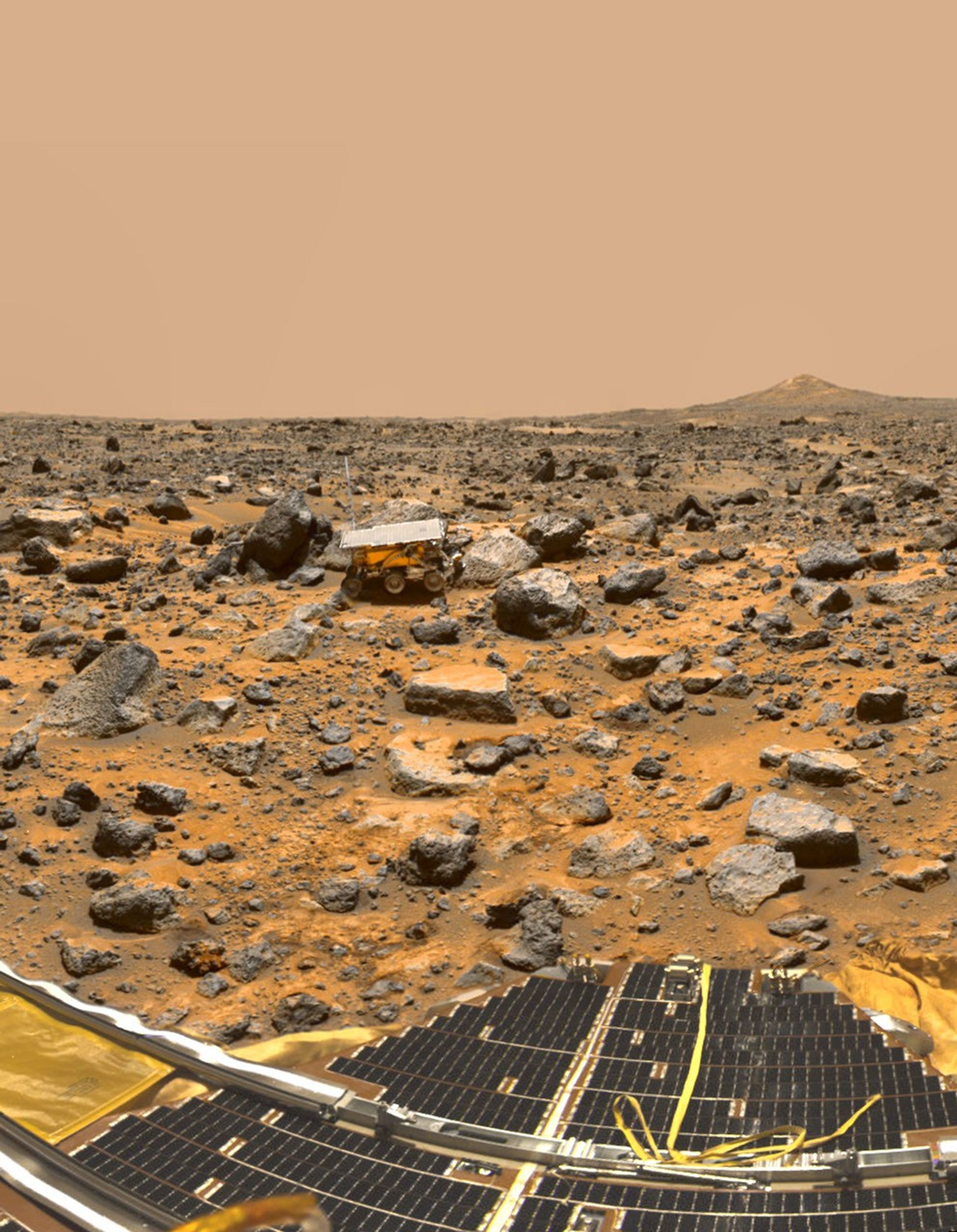 A small rover is in the distance among small rocks on Mars.