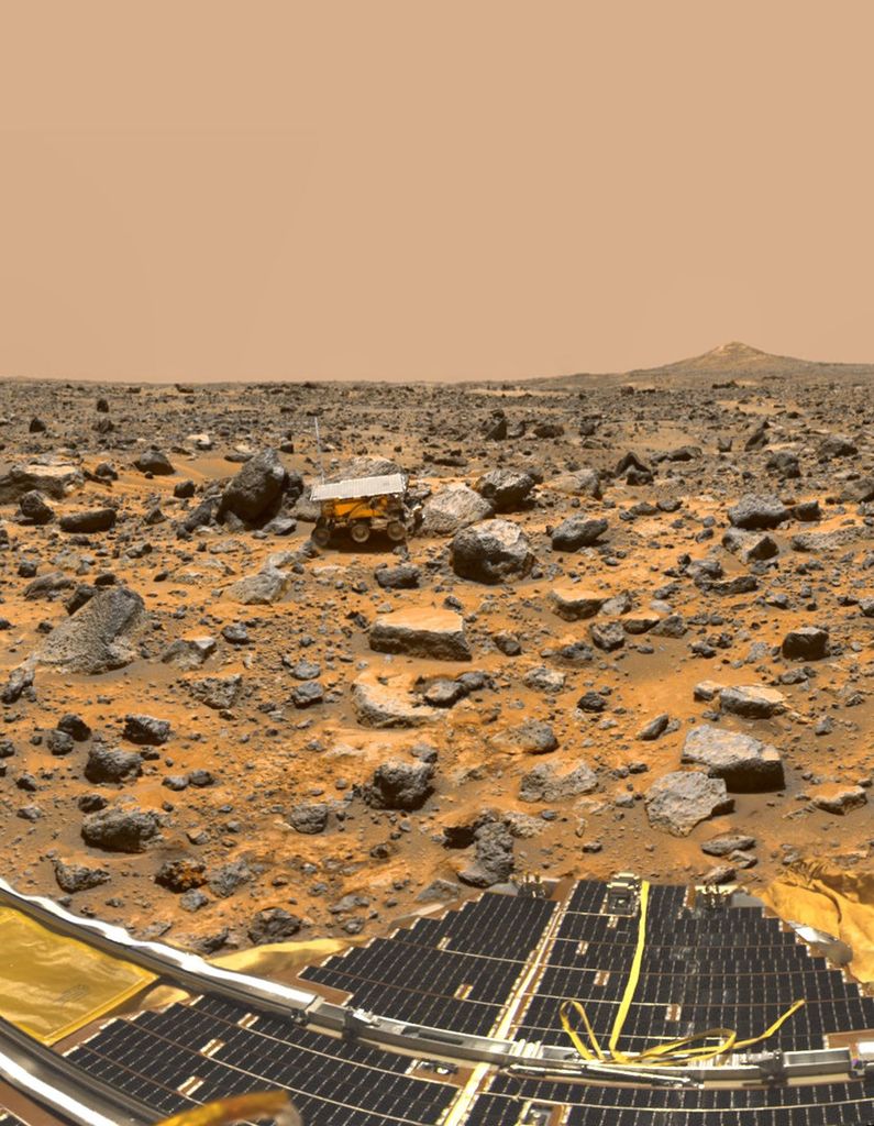 A small rover is in the distance among small rocks on Mars.