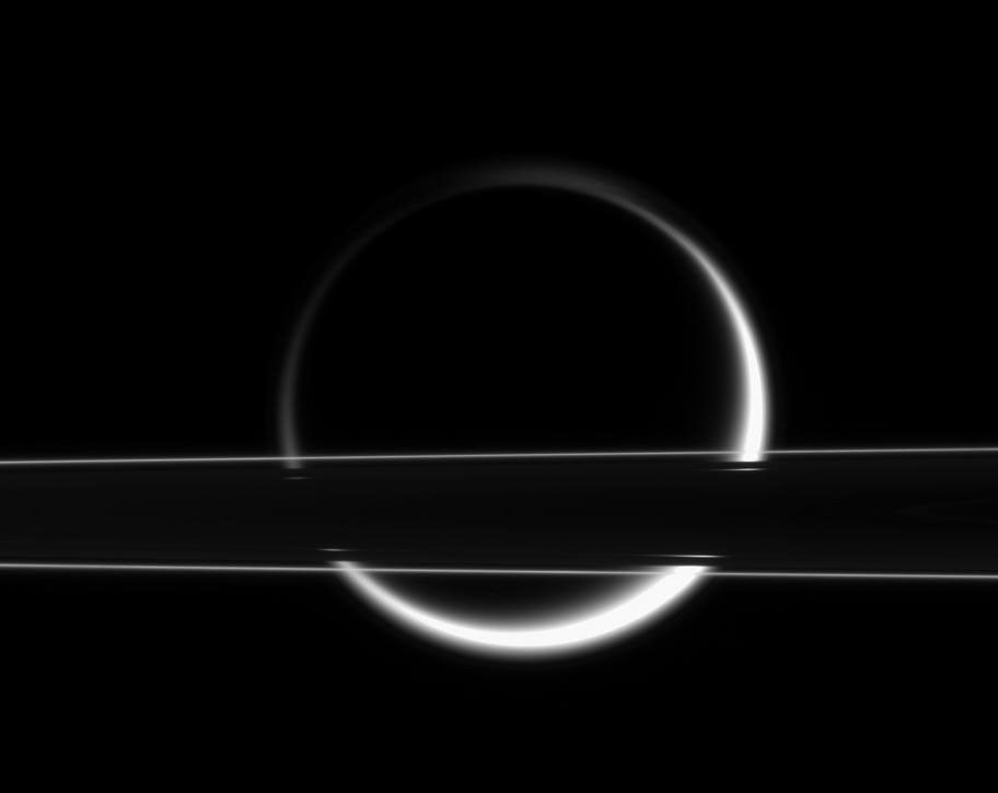 Titan's smoggy atmosphere glows brilliantly in scattered sunlight, creating a thin, gleaming crescent beyond Saturn's rings.