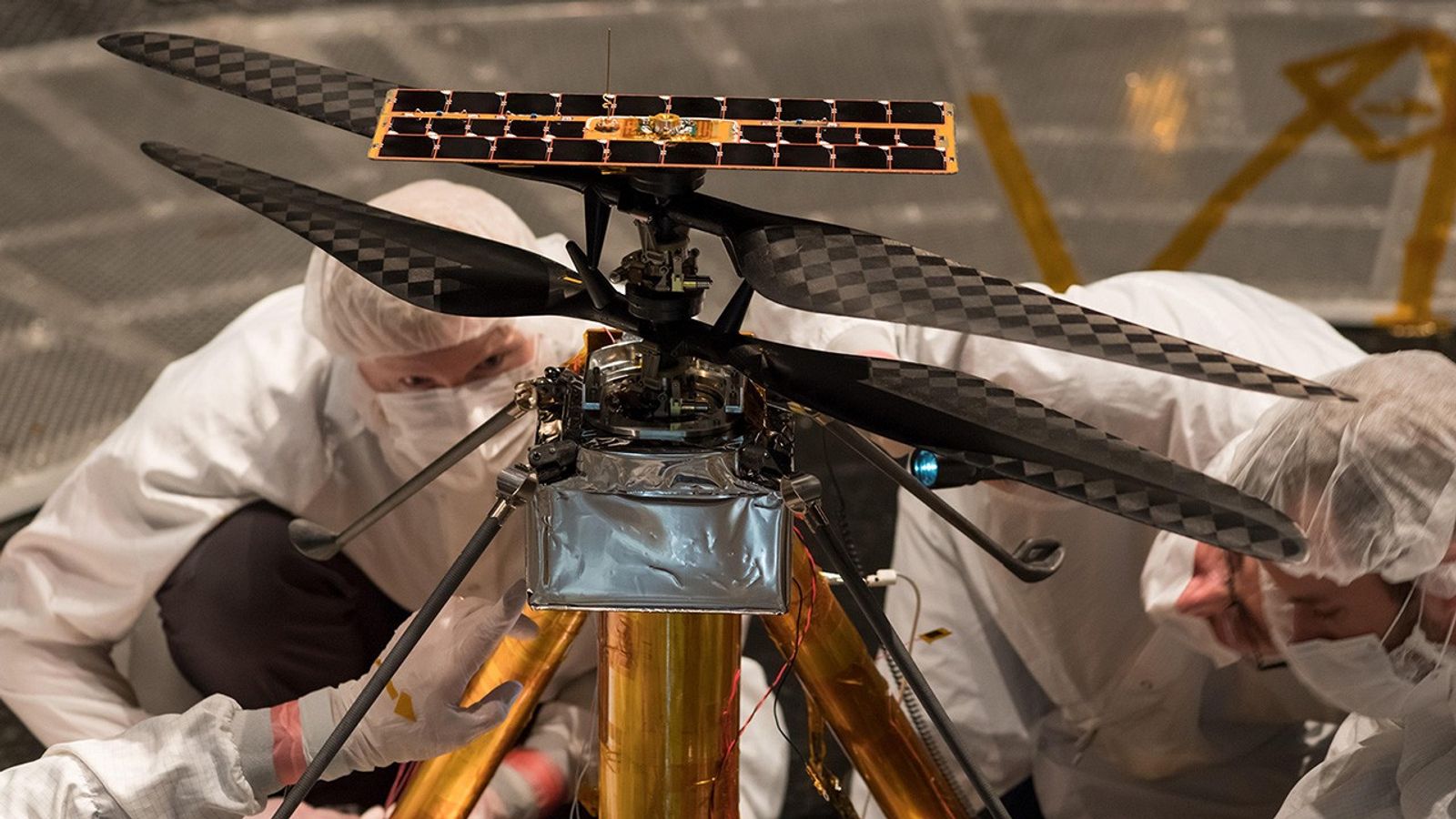 Engineers in clean suits inspect small helicopter.