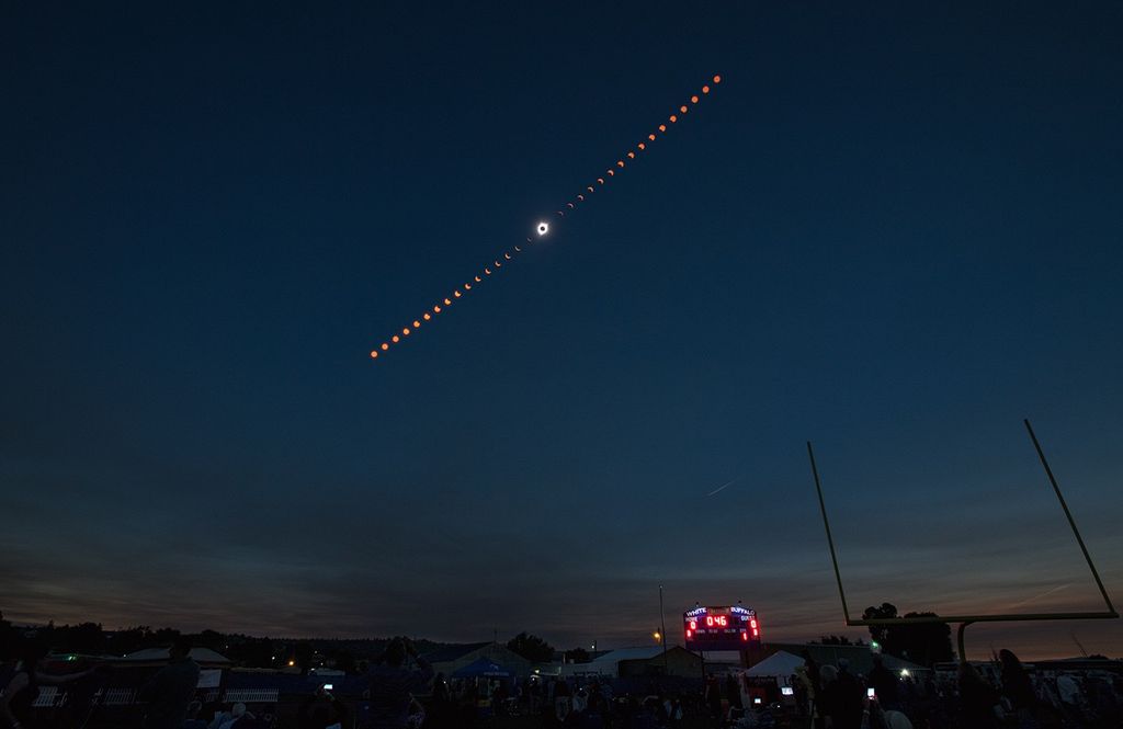 A timelapse shot of a total solar eclipse against a dark sky. The several phases of the eclipse show up like a dotted line across the sky, with an image of the total solar eclipse at the center.