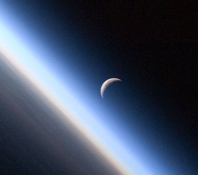 A setting, waning crescent moon amid the thin line of Earth's atmosphere.