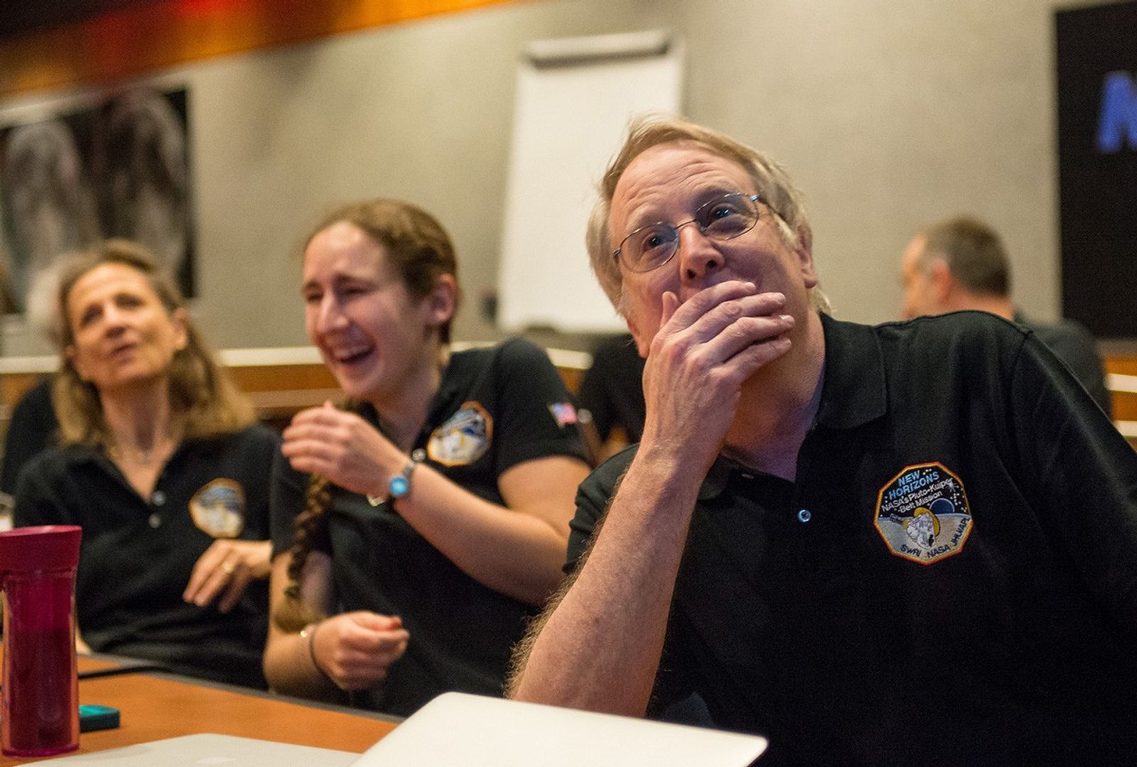 Two women and a man react with joy at seeing the first images of Pluto.