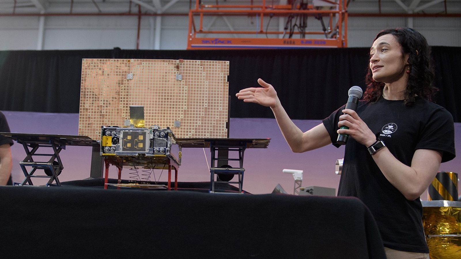 Woman explains the parts of a small satellite.