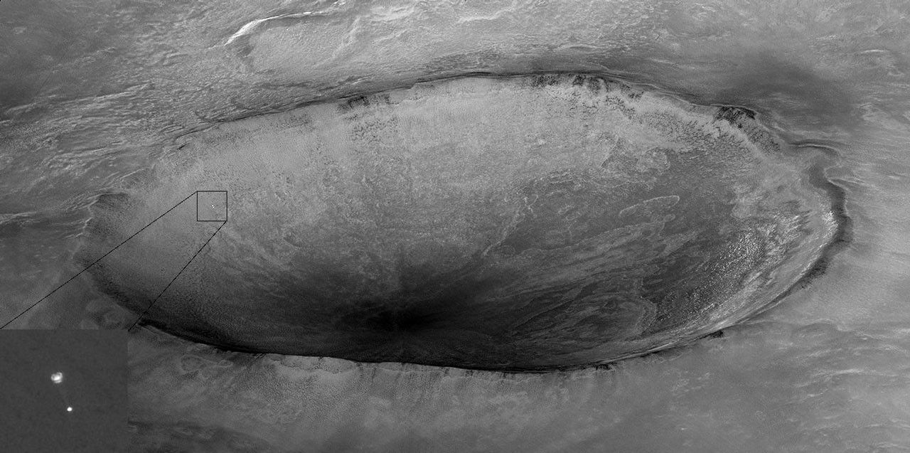 Spacecraft descending to Mars with large crater in background.