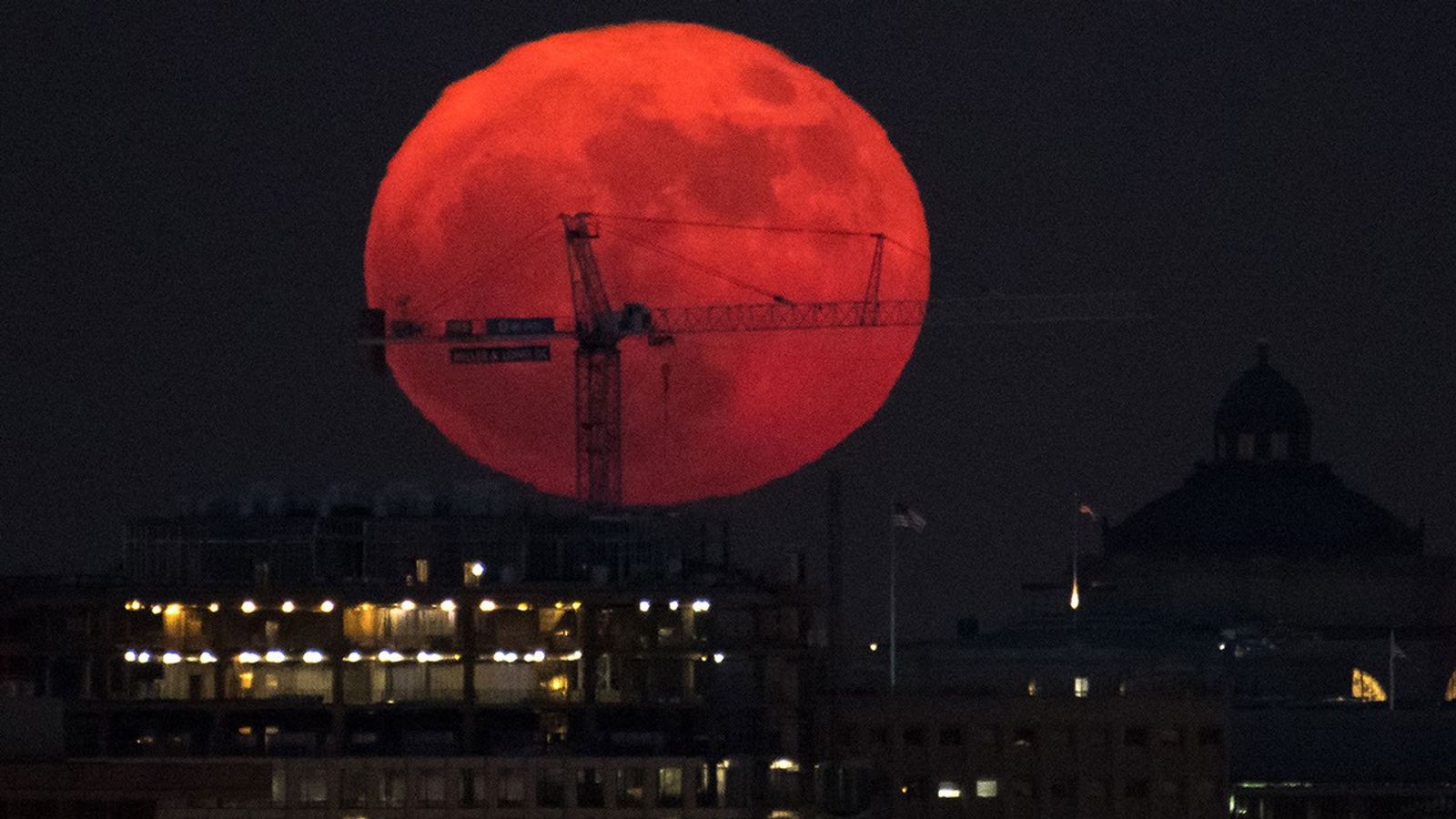 Large orange Moon rising behind crane on Washington skyline.