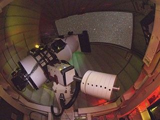 Large telecope pointed out on dome opening filled with stars.