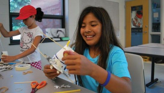 A child does a hands-on activity using a paper cup and other materials.