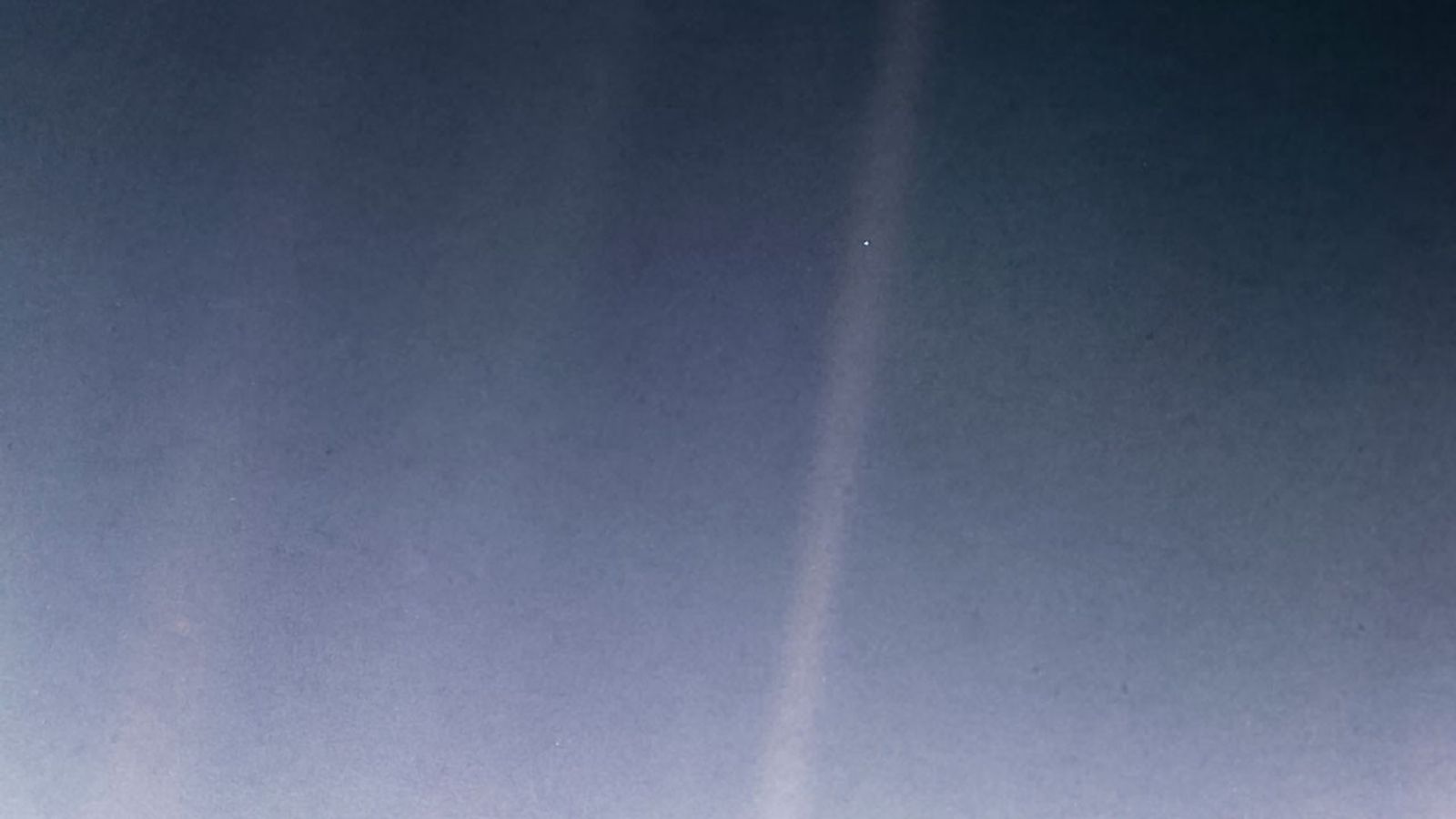 Distant view of Earth as a bright pale blue dot caught in a sunbeam.