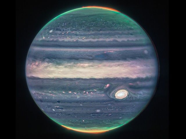 Auroras and hazes glow in this composite image of Jupiter. Since infrared light is invisible to the human eye, the light has been mapped onto the visible spectrum: the auroras are mapped to redder colors, hazes to yellows and greens, and light reflected from a deeper main cloud to blues. Jupiter's Great Red Spot is seen as a prominent yellow-white oval at the bottom right.