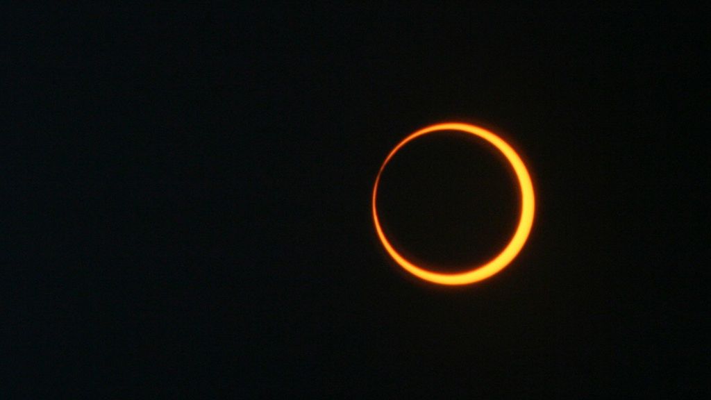 An annular eclipse showing the Sun's orange ring around the Moon's silhouette against a dark black sky