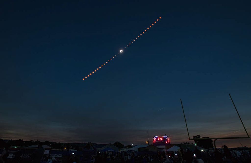 A twilight sky over a football field, showing the progression of a solar eclipse in a line across the sky, with totality in the middle of the line